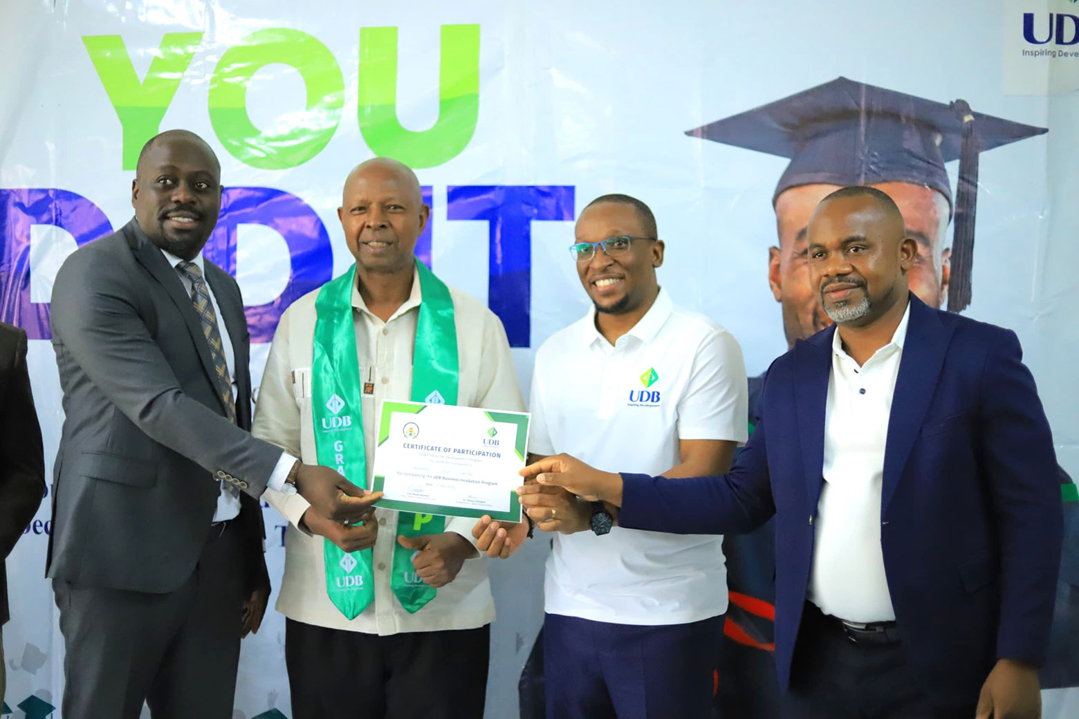 A graduate (2nd L) poses with UDB's Director Strategy and Corporate Affairs, Joshua Allan Mwesiga (2nd R), together with MUBS' Prof Richard Aki